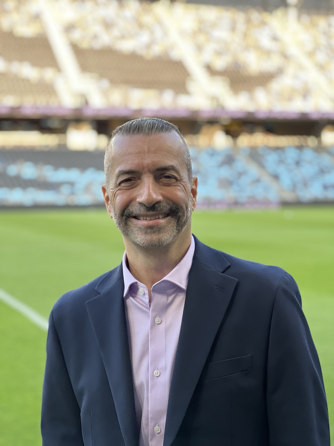 Daniel Chapela in a blue blazer beside the field